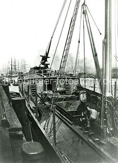 Historische Fotos aus dem Hafen Hamburgs; Spiritusfässer werden im Hansahafen über eine Schiffswinde in ein Hafenfahrzeug gelöscht.