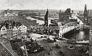 Eingespannte Zugpferde stehen mit ihren Fuhrwerken auf dem Messberg, die Kutscher warten auf der Strasse auf eine Fuhre. Auf der Wandrahmsbrücke über dem Zollkanal warten die Pferdefuhrwerke.