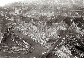 historisches Flugbild von Hamburg; unten fährt gerade ein Zug über die Oberhafenbrücke Richtung Hamburger Hauptbahnhof. Neben den Bahngleisen die Deichtorhalle - auf dem Gelände findet der Gemüsemarkt statt.