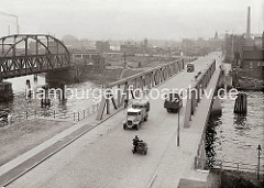 Blick über den Reiherstieg vom Kleinen Grasbrook nach Steinwerder; mit Fässern beladene Lastwagen, Fahrradfahrer und ein Motorrad mit Beiwagen überqueren die Reiherstiegbrücke. Links die Eisenbahnbrücke über den Reiherstieg.