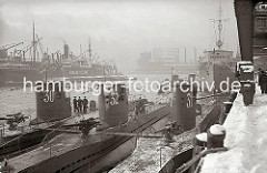 Drei U-Boote liegen nebeneinander am Versmannkai vor den Fruchtschuppen des Baakenhafens; der Kai ist mit Schnee bedeckt. Im Hintergrund ist das Gasometer beim Magdeburger Hafen zu erkennen.