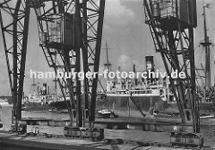 die Kräne im Hamburger Hafen laufen auf Schienen - im Vordergrund der Kai Breslauer Ufer im Oderhafen. Schiffe liegen auf Reede im Hafen; Schuten und Binnenschiffe haben an der Bordwand fest gemacht.