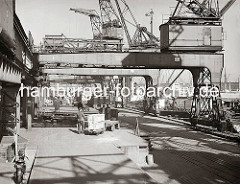 Ein Elektrokarren steht auf der Laderampe des Chilekais im Hamburger Oderhafen. Zwei Holzkisten sind auf dem Anhänger des Transportfahrzeugs von den Kaiarbeitern gestapelt worden. An der Laderampe steht ein mit Paketen voll beladener Güterzug.