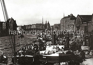 Breite Frachtkähne liege nebeneinander am Ponton des Hamburger Gemüsemarkts am Deichtor; die Ladung der Schiffe besteht aus Kisten, Körben und Holztonnen, in denen die Ware für den Markt angeliefert wird.