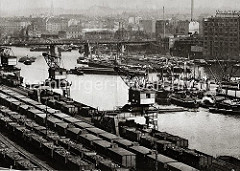 Dampffrachter und Binnenschiffe liegen im Billehafen; einige von den grossen Lastkähnen liegen in der Mitte des Hafenbeckens. Ein Hafenschlepper zieht vier mit Kohle hoch beladene Schute bei der Eisenbahnbrücke über das Wasser des Billehafens