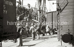 Feierabend bei Arbeitern im Hamburger Hafen - die Hafenarbeiter verlassen über die Gangway den Frachter am Roßkai. Die meisten Männer tragen die typische Hamburger Schirmmütze, den "Elbsegler" und einen Zampel. In diesem Beutel tragen sie ihre Verpf