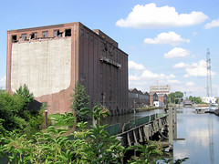 Ziegelwiesenkanal, alter Industriekanal im Hafengebiet in Hamburg Harburg; alter Bootssteg - am Kanalufer Wildwuchs. Der große Speicher am Kanal steht leer, die Fenster sind teilweise ausgebrochen - im Hintergrund die Klappbrücke  zum Harburger H