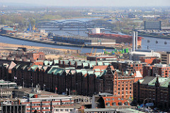 Blick über die Gebäude in der Hamburger Speicherstadt zur Norderelbe und den Norderelbbrücken. Ein Frachtschiff liegt am Kirchenpauerkai - davor das Hafenbecken vom Baakenhafen.