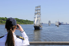 Fotos vom Hamburger Hafengeburtstag - Hochbetrieb auf dem Wasser und an Land; eine Offiziersanwärterin eines Segelschulschiffes beobachtet durch das Fernglas ander Schiffe auf der Elbe.
