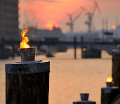 Feuerdekoration auf Holzdalben im Sandtorhafen - Eröffnung des Hamburger Traditionsschiffhafen im Sandtorhafen - Hafenkräne im Hintergrund, untergehende Sonne, roter Abendhimmel. (2008)