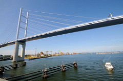 Rügenbrücke über den Strelasund bei Stralsund - Polygon mit Stahlseilen; ein Sportboot fährt unter der Brücke hindurch - Hintergrund der Hafen und die Altstadt von Stralsund
