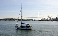 Blick vom Hafen Stralsunds auf die Rügenbrücke - ein Segelschiff fährt unter Motorkraft aus dem Stralsunder Hafen Richtung Ostsee.