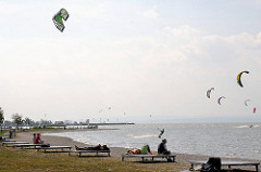 Strand vom Neusiedler See in Podersdorf - Kitesurfer nutzen den frischen Wind für Ihren Sport - Zuschauer sitzen auf Bänken in der Sonne.