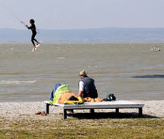 Strand vom Neusiedler See in Podersdorf - Kitesurfer nutzen den frischen Wind für Ihren Sport - Zuschauer sitzen auf Bänken in der Sonne.