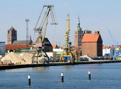 Hafenbereich der Hansestadt Stralsund - Kräne am Kai, Speichergebäude - im Hintergrund Kirchturm der St. Nikolaikirche und  St. Jacobikirche.