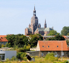 Kirchturm und Kirchenschiff der Stralsunder Marienkirche hinter Dächern von Gewerbehäusern des Stralsunder Hafengebiets.