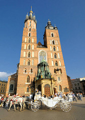 Türme der Marienkirche in Krakau / Kraków - die römisch katholische Basilika wurde vom 13. bis zum Beginn des 15. Jahrhundert, als klassisches Beispiel gotischer Architektur errichtet.  Eine weisse Kutsche mit weissen Pferden hält vor dem Eingang der
