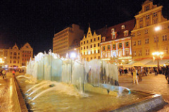 Springbrunnen am Abend auf dem Marktplatz von Wroclaw / Breslau in Polen; am Rande des Platzes historische und moderne Architektur.