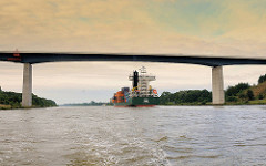 Brücke der A 23 über den Nord-Ostsee-Kanal; ein mit Containern beladenes Frachtschiff fährt unter der Brücke hindurch.
