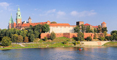 Blick über den Lauf der Weichsel - Wisla; Blick über den Fluss zur Wawel - Burgmauern und Türme der Kathedrale St. Stanislaus und Wenzel in Krakau / Kraków. Menschen in der Sonne in der Grünanlage des Weichselufers.