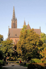 Die St. Michaeliskirche in Wroclaw, Brelau zwischen Bäumen - Parkbesucher gehen in der Sonne spazieren.