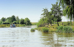 Landschaft an den Ufern der Krückau - Schafe weiden im dichten Gras, ein Sportboot fährt flussabwärts.