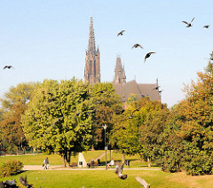 Die St. Michaeliskirche in Wroclaw, Brelau zwischen Bäumen - Parkbesucher gehen in der Sonne spazieren.