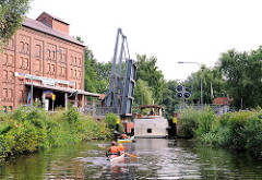 Die Klappbrücke vor der Schleuse „Findenwirunshier" ist hochgeklappt - ein Sportboot fährt in die Schleusenkammer ein - zwei Kanus warten.