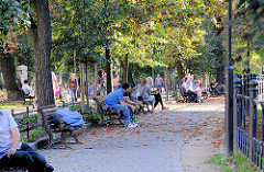 Grünanlage in Wroclaw, Breslau - Parkbesucher sitzen oder liegen auf Parkbänken in der Abendsonne.