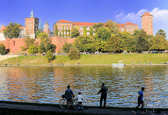 Angler und Jogger am Ufer der Weichsel - Wisla; Blick über den Fluss zur Wawel - Burgmauern und Türme der Kathedrale St. Stanislaus und Wenzel in Krakau / Kraków.