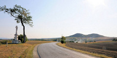 Einsame Landschaft - Baum alleinstehend, Steinkreuz auf einem Sockel am Strassenrand - Hügel im Hintergrund; Route Brno / Brünn.