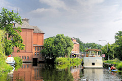 Historische Industriearchitektur in Neu Kaliß - ehem. Mühlengebäude, jetzt Wasserkraftwerk. Ein Sportboot fährt Richtung Schleuse „Findenwirunshier".