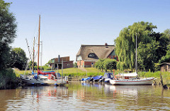 Sportboothafen am Ufer der Krückau - im Hintergrund ein reetgedecktes Wohnhaus am Deich.
