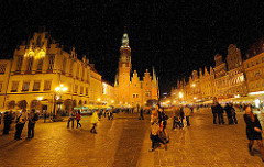 Marktplatz von Breslau / Wroclaw am Abend - Touristen gehen über das Kopfsteinpflaster auf dem Platz; im Hintergrund der Rathausturm und das historische Rathaus.