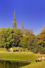 Die St. Michaeliskirche in Wroclaw, Brelau zwischen Bäumen - Parkbesucher gehen in der Sonne spazieren.