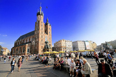 Touristen auf dem Hauptmarkt von Krakau - im Hintergrund Bürgerhäuser und die römisch katholische Marienkirche; sie wurde vom 13. bis zum Beginn des 15. Jahrhundert errichtet.