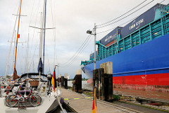 Ein mit Containern beladenes Frachtschiff fährt aus der Schleusenkammer Schleuse Brunsbüttel in den Nord-Ostsee-Kanal ein - lks. Sportboote im Yachthafen an der Schleuse.