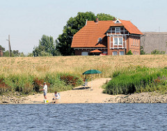 Wohnhaus hinter dem Deich - Sandstrand an der Elbe - Angler in der Morgensonne am Wasser