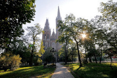 Park, Grünanlage der St. Michaelis Kirche Wroclaw, Breslau - Polen; die tiefstehende Sonne scheint durch die Bäume.