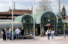 Moderner Eingang vom Bahnhof Uelzen - Passanten und Fahrgäste; im Hintergrund das historische Bahnhofsgebäude, das 2000 nach Plänen des österreichischen Künstlers Friedensreich Hundertwasser umgebaut wurde.