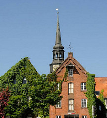 Historische Speicher mit Efeu bewachsen am Hafenrand von Stade - Kirchturm der St. Cosmaekirche.