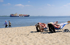 Elbufer bei Stade / Containerschiff auf der Elbe - Strandbesucher in Liegen / Liegestühle im Sand in der Sonne - Spaziergänger.