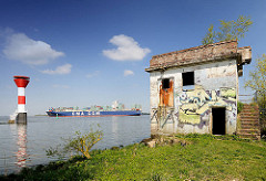 Elbufer beim Stader Sand - altes Gebäude mit Graffiti; Leuchtfeuer und Frachtschiff auf der Elbe.