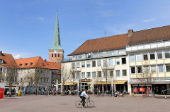 Herzogenplatz in Uelzen - ein Fahrradfahrer fährt über den leeren Platz - Aussengastronomie, Tische in der Sonne am Rande des Platzes - im Hintergrund der Kirchturm der St. Marienkirche.