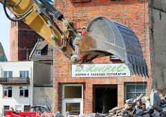 Abriss von Gebäuden in der Mühlenstrasse - Abrissbagger und Bauschutt. Baggerschaufel und Firmenschild eines Abrissgebäudes - W. Henkel Moped Fahrrad Reparaturen.