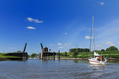 Segelboot unter Motor auf der Schwinge - Schwingesperrwerk, geöffnete Klappbrücke, blauer Himmel.