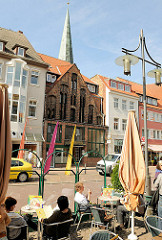 Eiscafé am Strassenrand - Tische mit Gästen in der Sonne; im Hintergrund das im Mittelalter errichtet Gildhaus und die Turmspitze der St. Marienkirche.