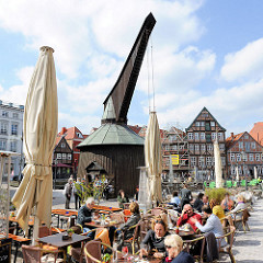 Sonnentag in Stade - Café mit Tischen und Sitzplätzen auf dem Fussweg - historischer Holztretkran / Alter Kran am historischen Hansehafen.