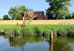 Ufer der Schwinge bei Brunshausen - alte Eisenleiter und Dalben - hinter dem Deich das Vereinhaus eines Ruderclubs.