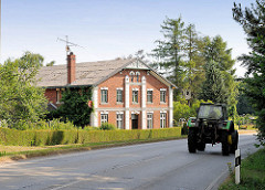 Wohnhaus eines Bauernhofs an der Lübecker Strasse in Ammersbek - ein Traktor fährt auf der Landstrasse.